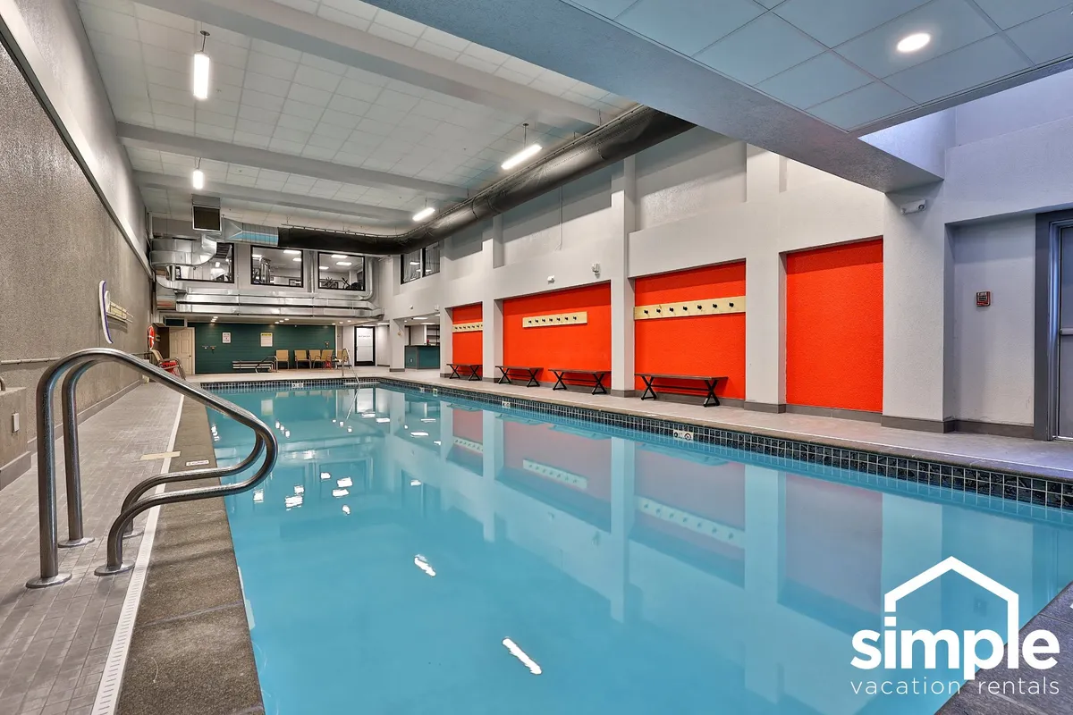 An inviting indoor swimming pool with brightly colored accent walls and poolside benches. The space feels active and relaxing, offering a hint at the après-ski amenities available to guests.