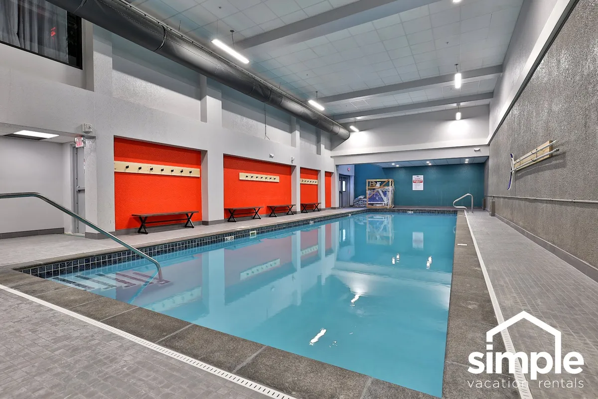 An inviting indoor swimming pool with vibrant accent walls, benches lining the poolside, and guests enjoying a refreshing swim or relaxing nearby. The space feels energetic and perfect for unwinding after a day on the slopes or trails.