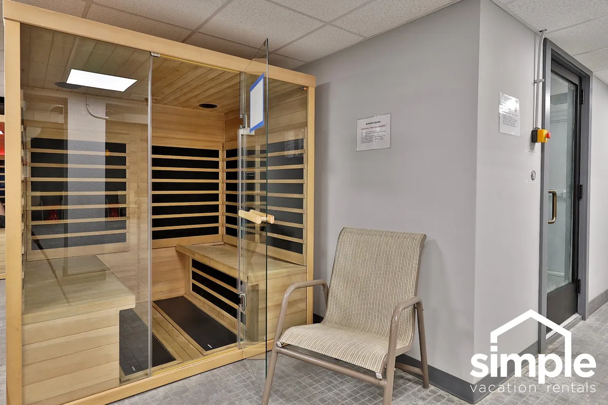 A calm, modern sauna space with glass walls, wooden benches, and a woven chair, radiating warmth and serenity. The subdued lighting fosters a sense of post-adventure recovery and wellness.