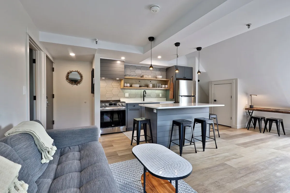 A stylish living space with a contemporary sofa facing a large kitchen island and bar stools. The decor features a decorative mirror and a wooden table, suggesting an area perfect for casual meals, entertaining, or planning adventures.