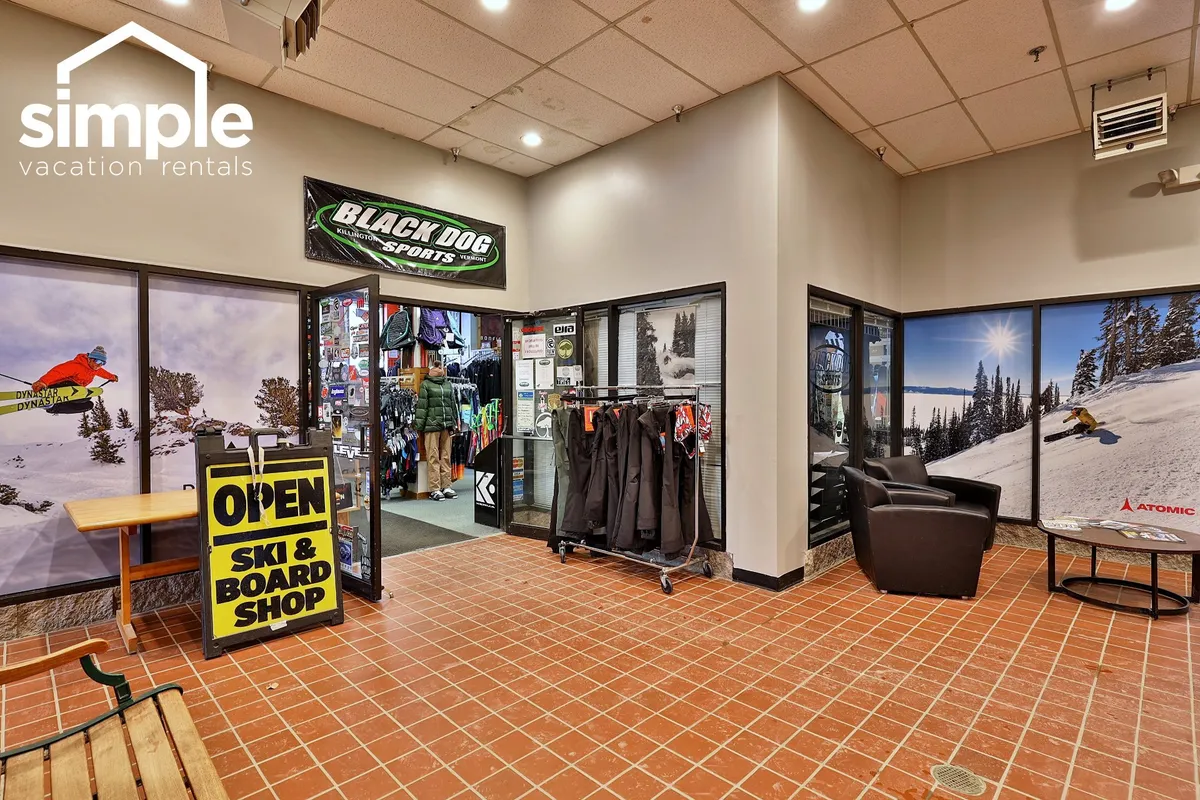 The entrance to the resort’s ski and snowboard shop, with a display of gear and a seating area where guests can gather, socialize, or get ready for an adventure on the slopes. The mood is excited and adventurous, perfect for guests preparing for a day outdoors.