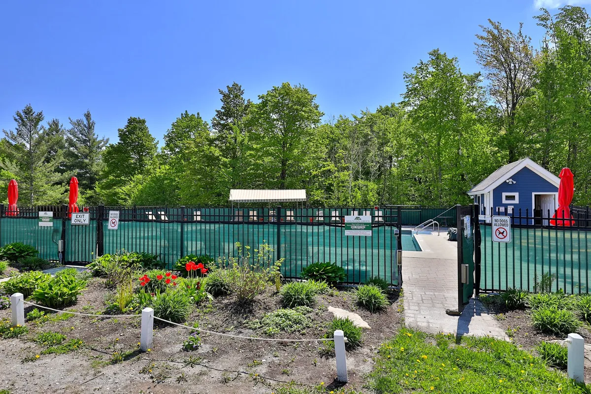 This exterior image features a sparkling swimming pool surrounded by a lush garden, red umbrellas, and a vibrant blue building. The setting suggests a lively yet relaxing atmosphere, ideal for unwinding after outdoor winter adventures. Lounge chairs and the inviting pool hint at the property's resort amenities.