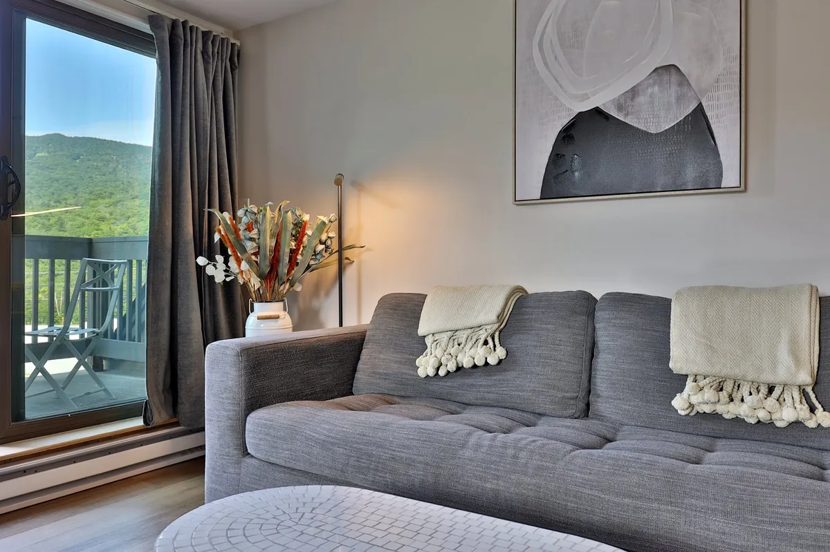 A cozy living room scene featuring a comfortable sofa, elegant artwork, a vase of fresh flowers, and soft curtains framing a window view. The space evokes a relaxing atmosphere perfect for unwinding after exploring Killington.