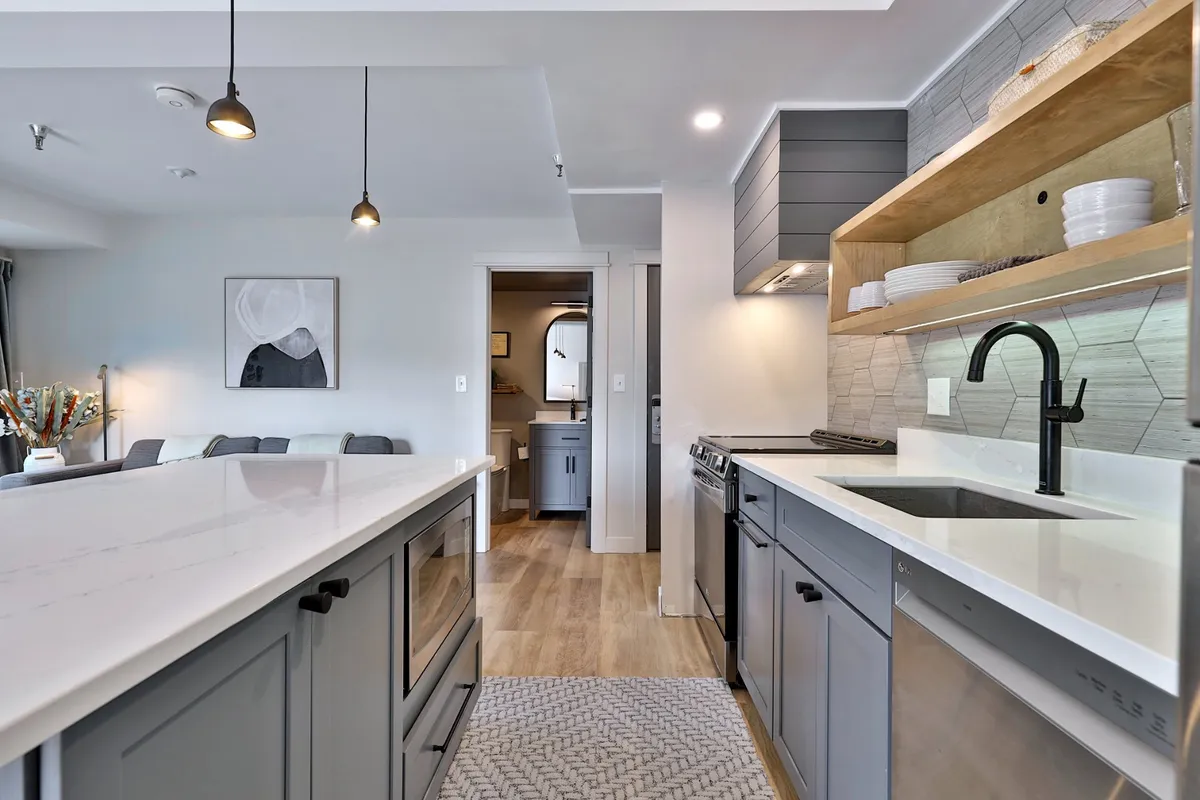 A contemporary kitchen scene highlighting a large island, stainless steel appliances, open shelving, and decorative artwork. The space feels open and connected to the living area, suggesting a seamless flow for entertaining and family interactions.