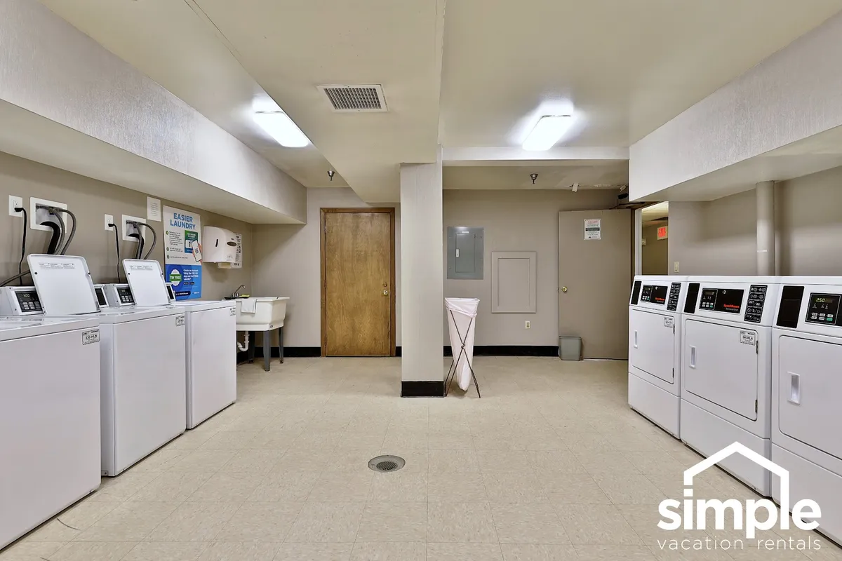 A practical laundry facility is shown with multiple washing machines, dryers, a utility sink, and a folding area, all set in a clean, functional space. The neutral decor focuses attention on convenience and the ease of handling daily chores.